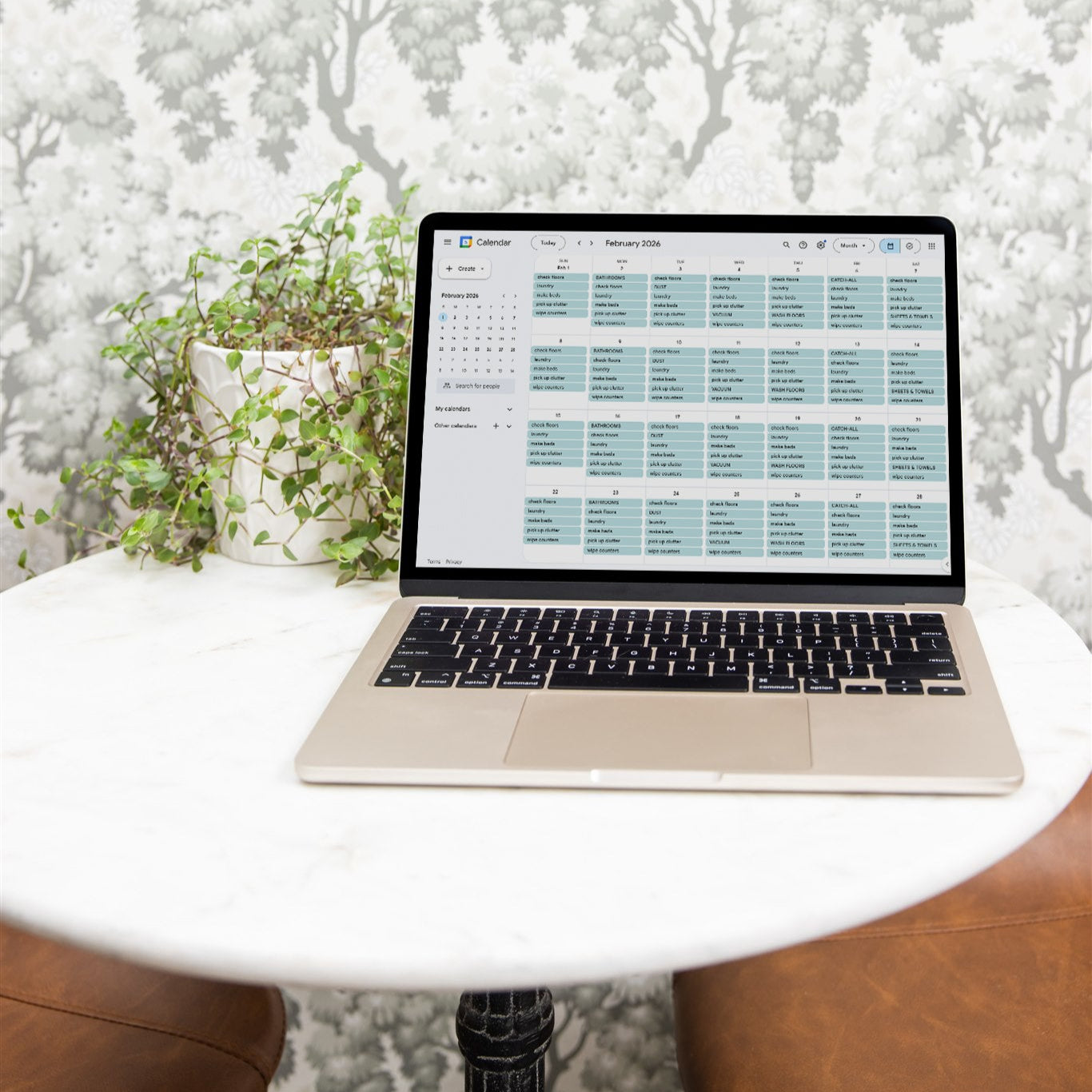 Laptop on a small round table with a white floral wallpaper background